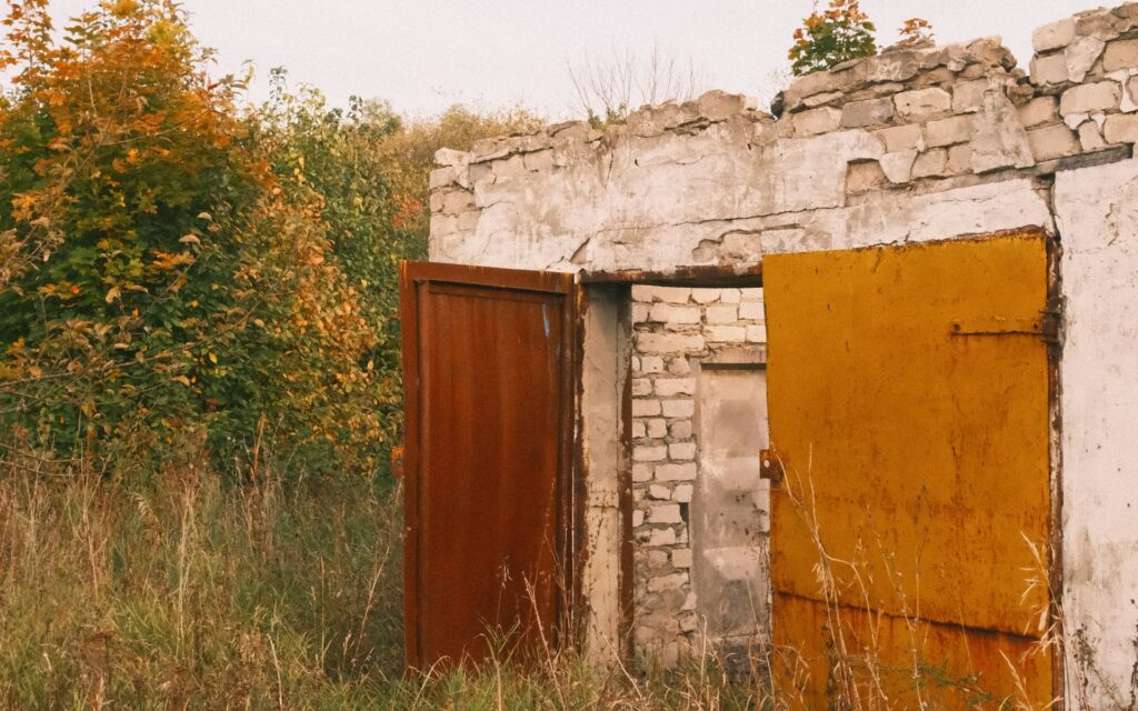 Bâtiment abandonné au milieu des herbes hautes, portes grandes ouvertes